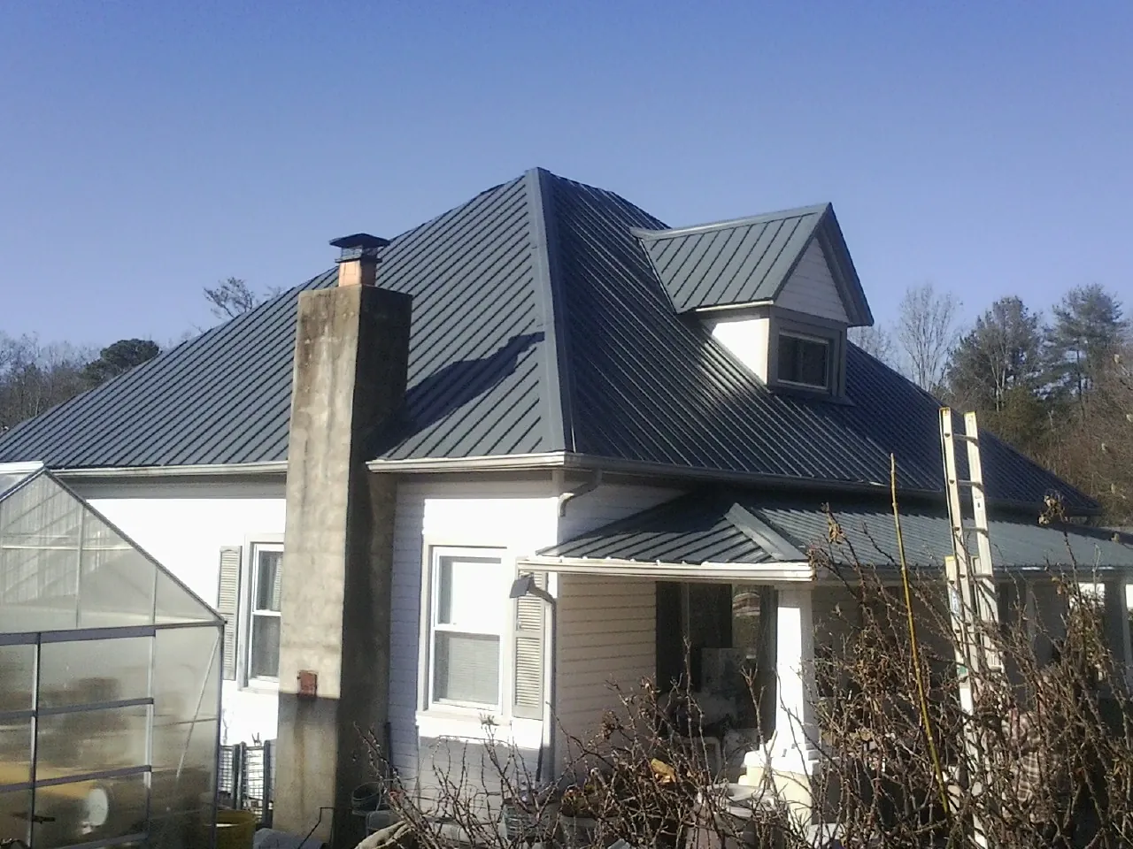 Dark blue standing seam metal roof on a white farmhouse with dormer — Slate & Tile Roof Repair by Roofing Brothers in Durango