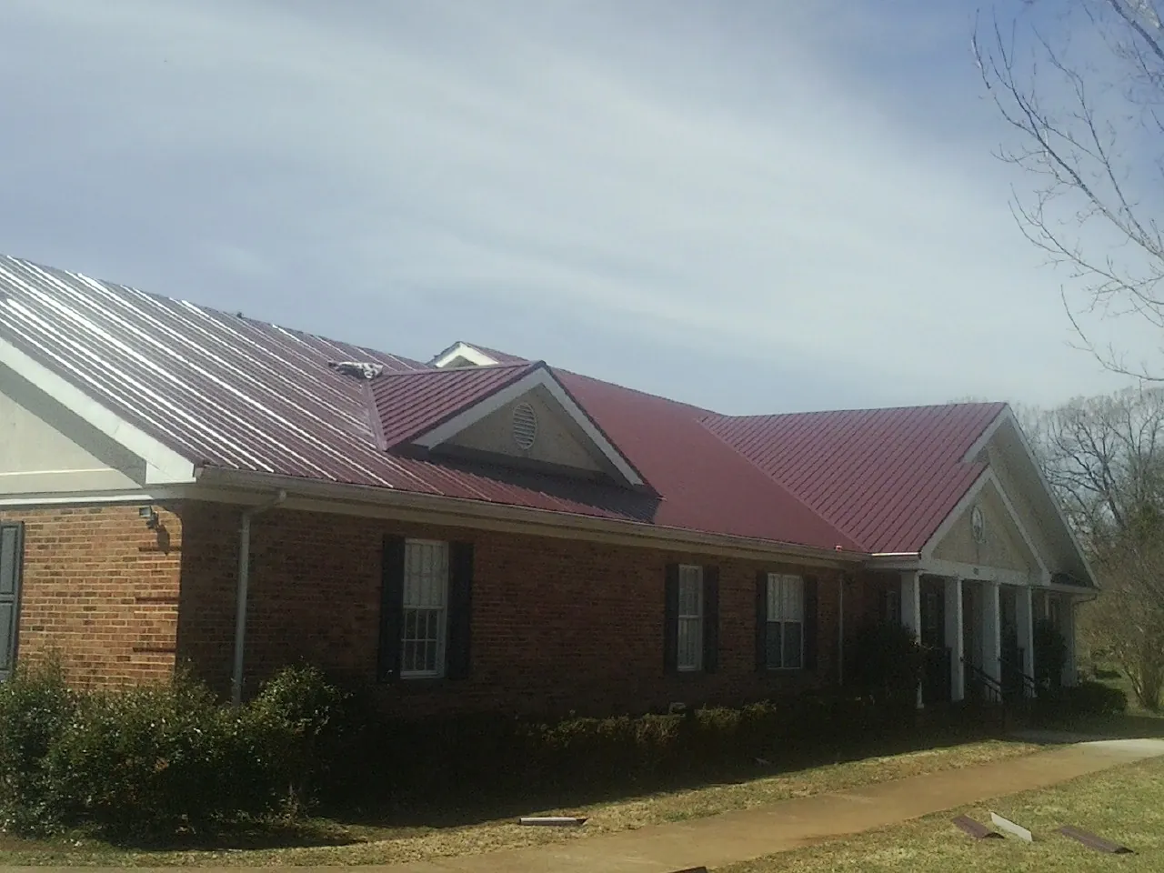 Red metal roof with gabled entries on a long brick building, from a Hail Damage Roof Repair job in Durango